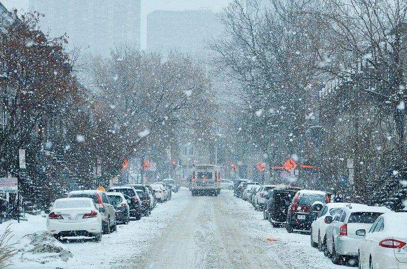 A snowy city street with cars parked on either side